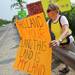 Dei Jillespie, of Ypsilanti, holds a sign as she rallies along a guard rail near Camp Take Notice as a means to promote awareness and raise funds for the camp during a rally along Wagner Road on Thursday.  Melanie Maxwell I AnnArbor.com